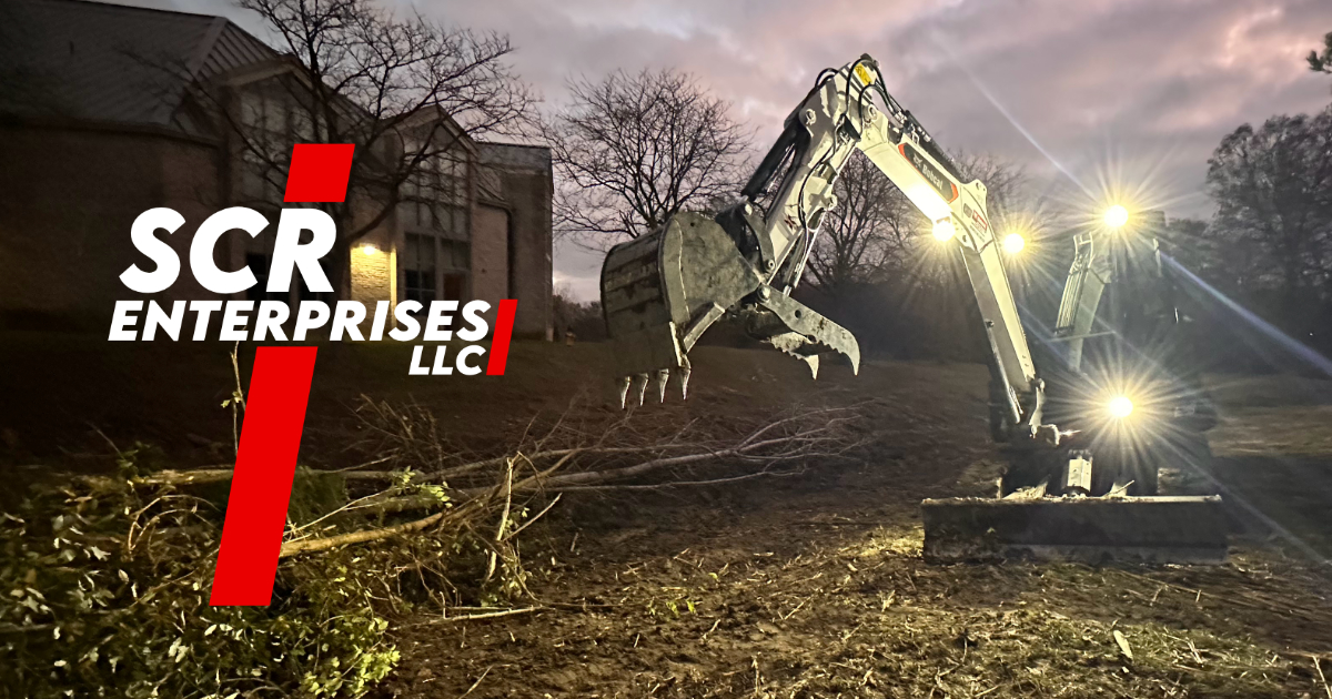 Excavator clearing land at night with lights on